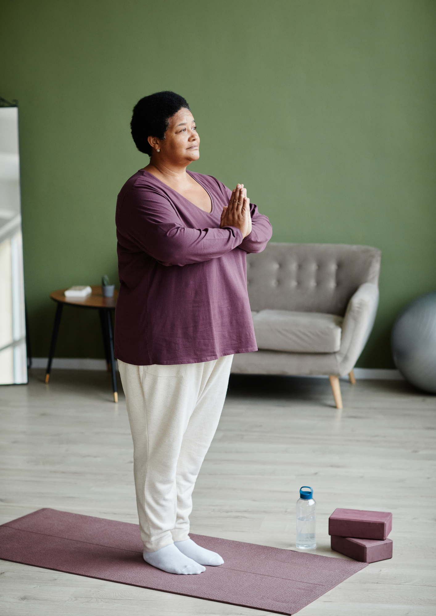 Frau steht zuhause auf einer Yogamatte in Namaste-Haltung